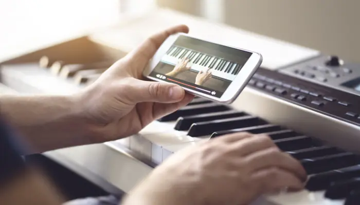 mains qui tiennent un smartphone avec une vidéo pour apprendre le piano en ligne au dessus d'un clavier